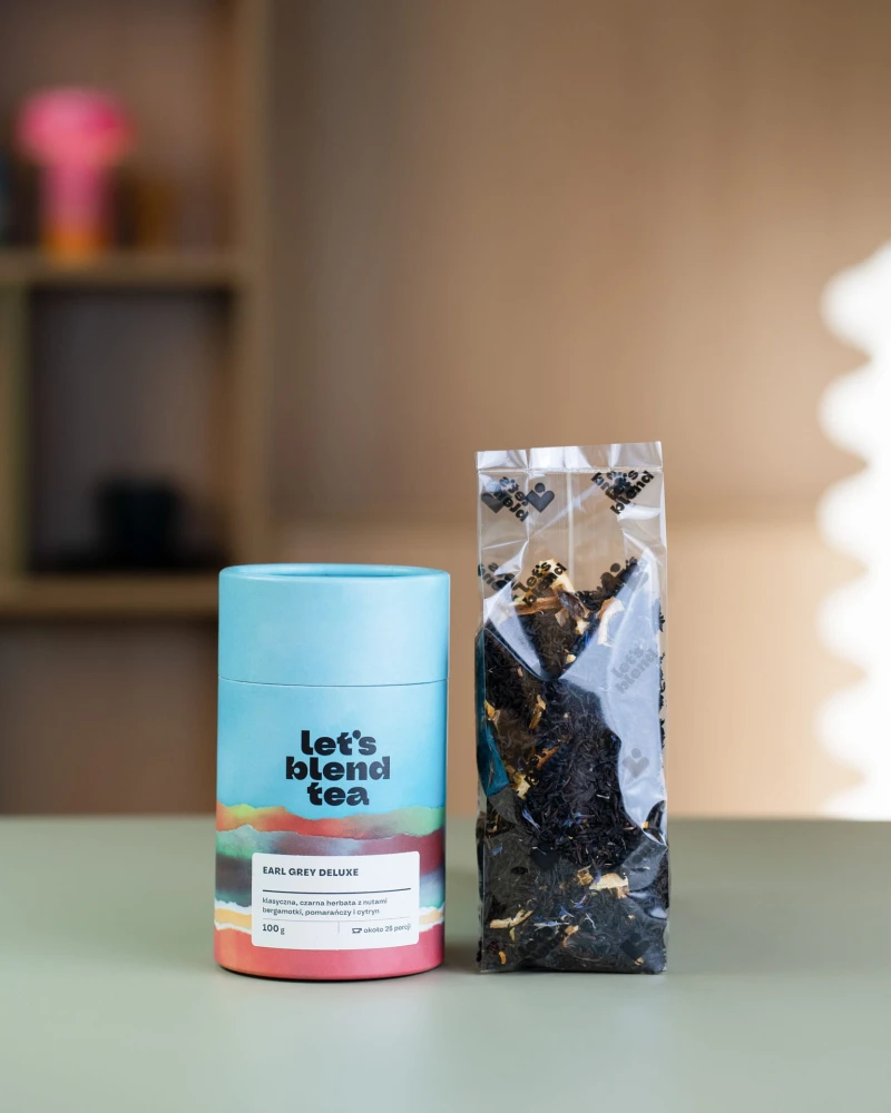 Tuba czarnej herbaty Earl Grey Deluxe Let's Blend obok otwartej torebki z liśćmi herbaty